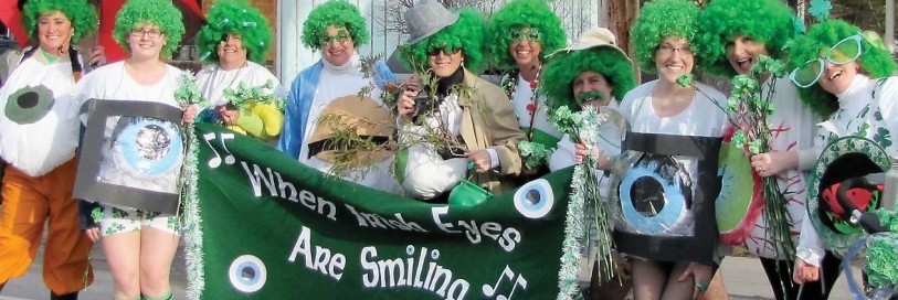 People in a line smiling with green wigs and st Patricks day items holding a green banner that say when Irish eyes are smiling